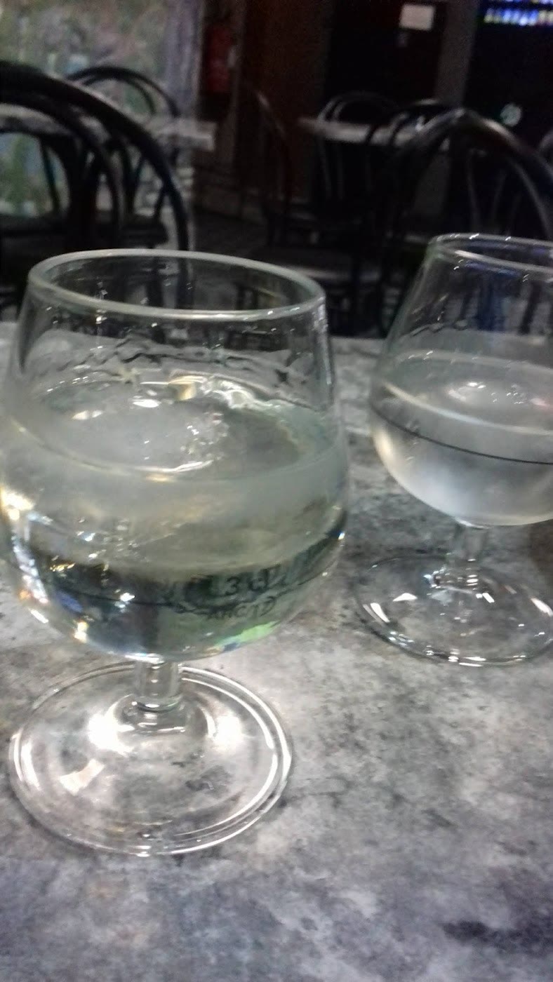 Dois copos numa mesa de mármore, de dia, com as cadeiras do café atrás